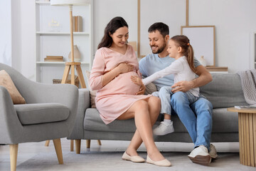 Little girl with her father touching pregnant mother's belly at home