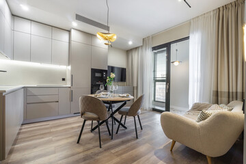 A contemporary kitchen and dining space showcase sleek cabinetry and a cozy seating arrangement, flooded with afternoon sunlight through large windows, creating a warm, inviting atmosphere.