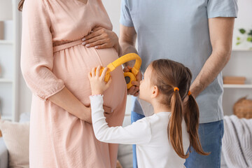Cute little girl putting headphones to her pregnant mother's belly and father at home
