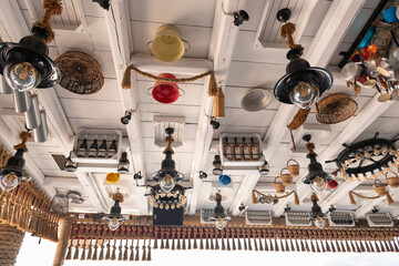 Eclectic ceiling decor in a Greek island restaurant with hanging lamps, baskets, and kitchen items.