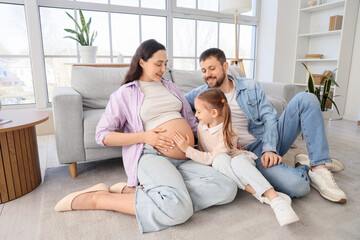 Cute little girl with her pregnant mother and father sitting on floor at home