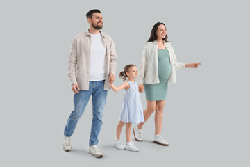 Fototapeta premium Cute little girl with her pregnant mother and father walking on light background