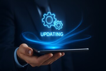A businessperson’s hand holds a tablet projecting a glowing gear icon with “updating” text above. Concept of software maintenance and continuous improvement.