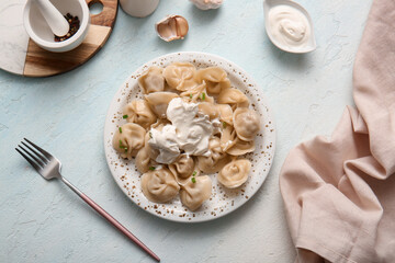 Plate of delicious boiled dumplings with sour cream and garlic on light blue background