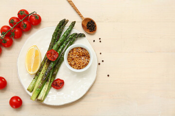 Plate with fried green asparagus, lemon and cherry tomatoes on white wooden background