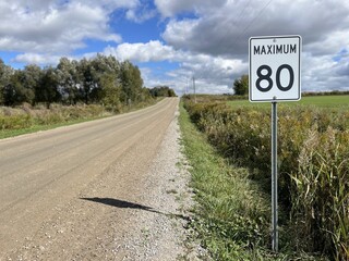 Rb-1 · Maximum 80 sign on a dirt road with a cloudy blue sky - Rb-1 - Panneau "Maximum 80" sur un chemin de terre avec un ciel bleu nuageux