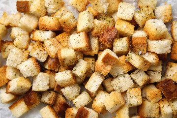 Crunchy croutons with spices on baking paper, closeup
