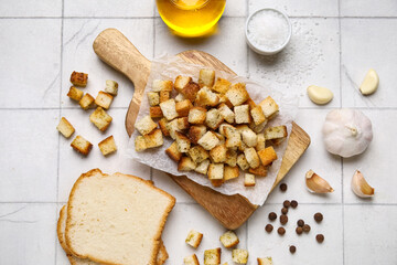 Wooden board with crunchy croutons and different spices on white tile background
