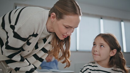 Smiling teacher talking child girl at table in classroom closeup. Pupil lesson