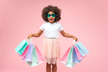 Light colored studio portrait of excited girl wearing styling sunglasses posing over pastel pink...