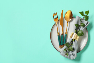 Beautiful table setting with golden cutlery and tree branch on turquoise background