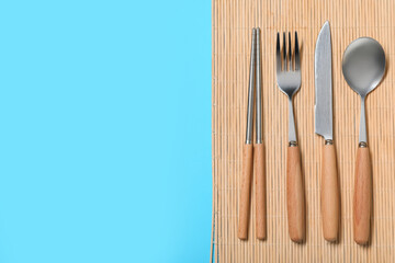Stylish silver cutlery and bamboo mat on blue background