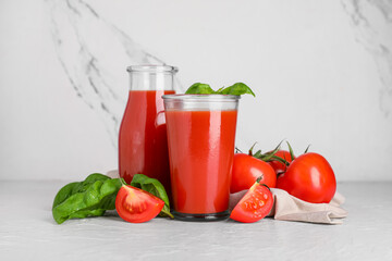 Glass and bottle of fresh tomato juice with basil on white background