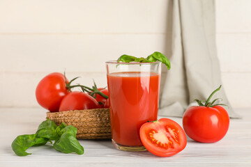 Glass of fresh tomato juice with basil and vegetables on white wooden background