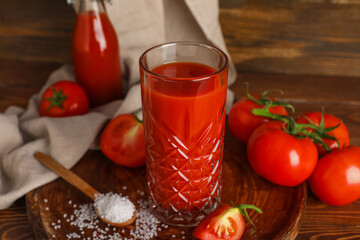Glass of fresh tomato juice and spoon with salt on wooden background