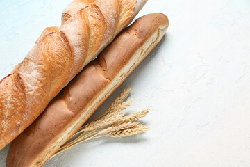 Fresh baguettes and wheat on light blue background, closeup