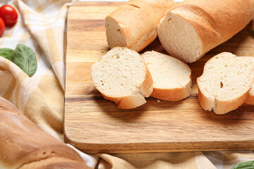 Wooden board with cut fresh baguette and basil on napkin, closeup