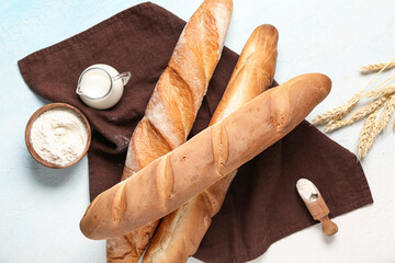 Fresh baguettes with wheat, flour and jug of milk on light blue background