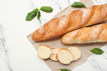 Paper with fresh baguettes and basil on white background