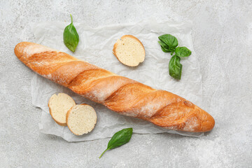 Baking paper with fresh baguette and basil on grey background