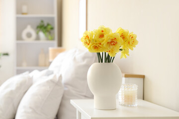 Vase with bouquet of beautiful narcissus flowers on bedside table in bedroom, closeup