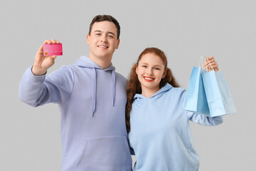 Beautiful young woman with shopping bags and her boyfriend holding credit card on grey background