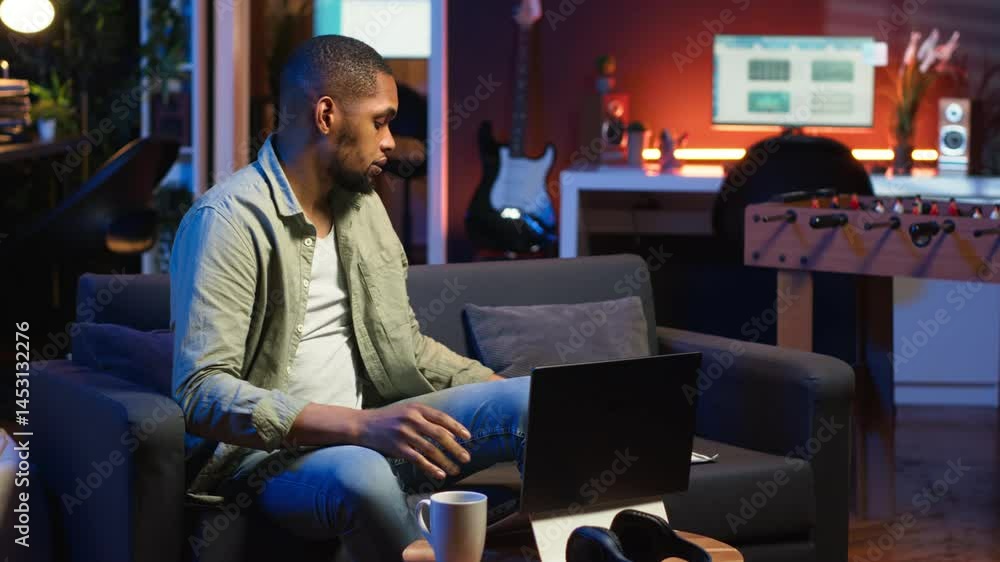 Poster african american guy does research by reading articles and data driven papers in the living room, us