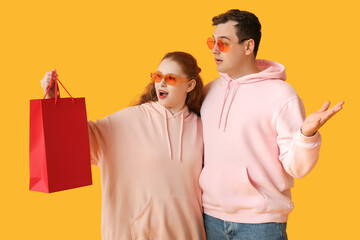 Surprised young couple with red shopping bag on yellow background