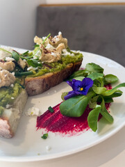 A vibrant breakfast plate featuring creamy avocado and spiced hummus on artisan bread, elegantly topped with edible flowers. Perfect for food blogs and upscale café menus.