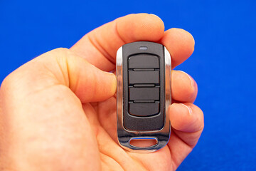 four-button remote control for opening garage doors held in hand on blue background