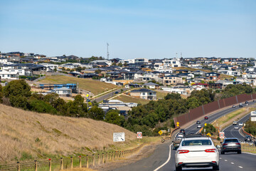 Traffic flowing into a modern hillside residential estate in Geelong, Australia, themes of suburban expansion, infrastructure development, and growing regional urbanization.
