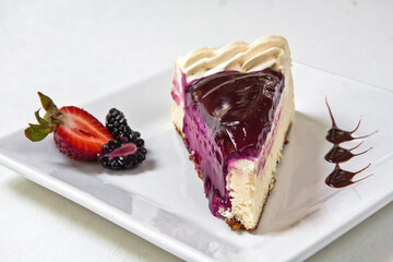 Cheesecake topped with blackberry sauce decorated with red berries and custard on a white background, slice of cake