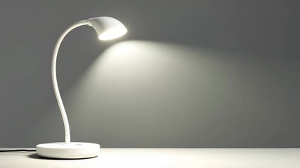 White desk lamp illuminates a gray background, casting a warm light. The lamp has a flexible neck and a modern design. Minimalist and clean aesthetic.