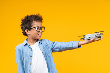 Studio shot of casually dressed African American schoolboy posing over yellow background with generic design drone in his hand, science, technology, modern education concept