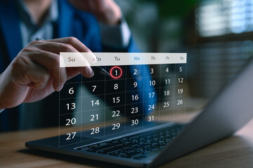 Businessman scheduling a digital calendar on laptop, highlighting the first of the month,...