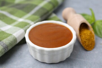 Tasty curry sauce, powder and basil leaves on grey table, closeup