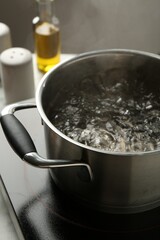 Cooking pot with boiling water and stove on table against grey background, closeup