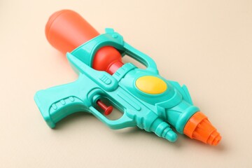 Bright plastic water gun on beige background, closeup