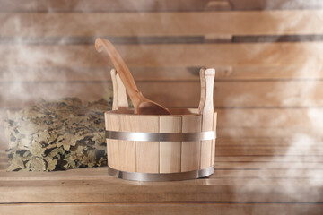 Bucket with ladle and whisk on wooden bench surrounded by steam in sauna