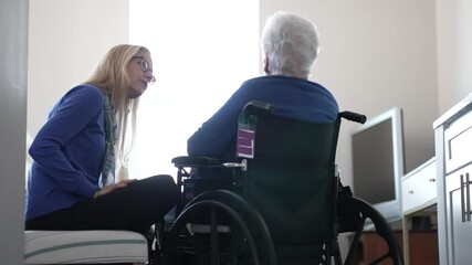 A woman in her nineties sits in a wheelchair, receiving heartfelt attention from her daughter. The cozy indoor setting highlights their close bond.