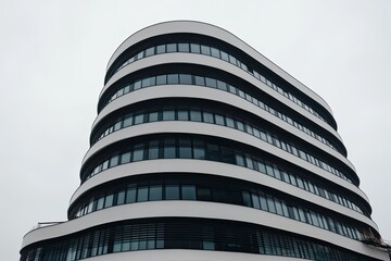 Modern, curved office building against a light gray sky  Curved facade with rows of windows, creating a unique architectural design