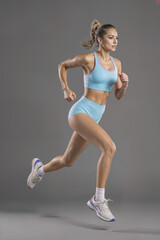 A beautiful woman runs in a light blue sports bra, light blue shorts and white sneakers. a plain gray background.