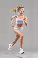 A beautiful woman runs in a light purple sports bra, light blue shorts and white sneakers. a plain gray background.