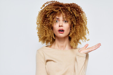 Surprised woman with curly blonde hair expressing shock against a light background Her wide eyes...