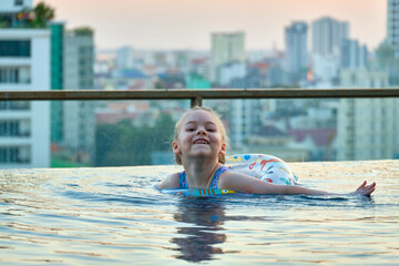 A beautiful little girl swims in a pool with an inflatable circle on the roof of a skyscraper in...