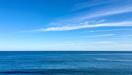 Obraz premium Calm Blue Ocean Meets a Bright Blue Sky with Wispy Clouds