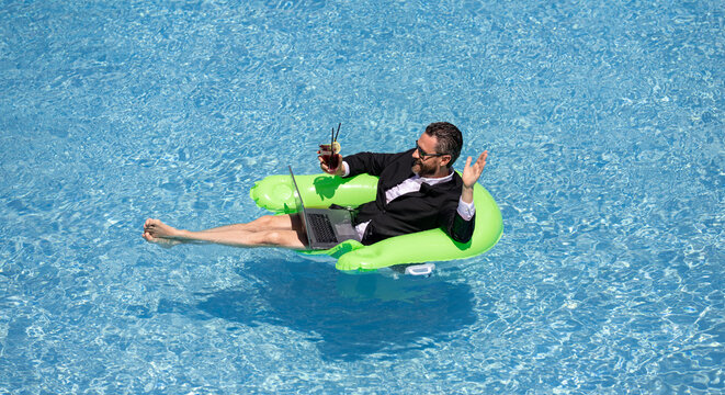 Funny business man in suit drink summer cocktail and using laptop on the sea beach. Summer holiday, outdoor and summer business travel concept. Crazy office worker dreams on summer at poolside.