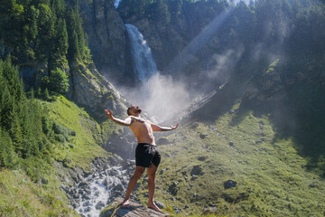 Carefree man in waterfall. Man freedom in waterfall landscape. Muscular man breathing fresh air on beauty waterfall. Topless model with raised hands on mountain nature landscape. Yoga by waterfall.