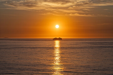 Cruise ship on the horizon, sunrise with orange sky directly above a ferry boat in the center