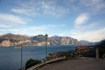 Road over the sea bay of the resort town. Road signs and lampposts are installed above the road. Mountains in the distance under the blue sky. Travel photo from vacation
